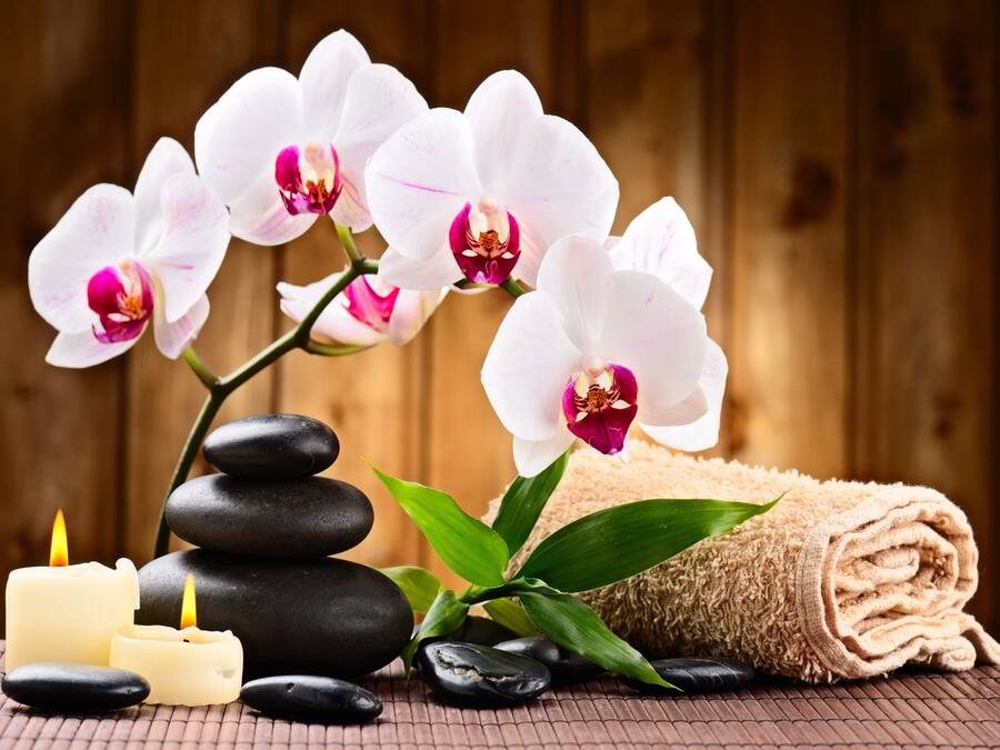 A stack of smooth, polished stones, a rolled beige towel, and white orchids with pink centers.