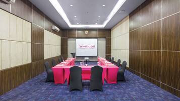 A conference room with a long table, chairs, a projector screen, and an air conditioning unit.