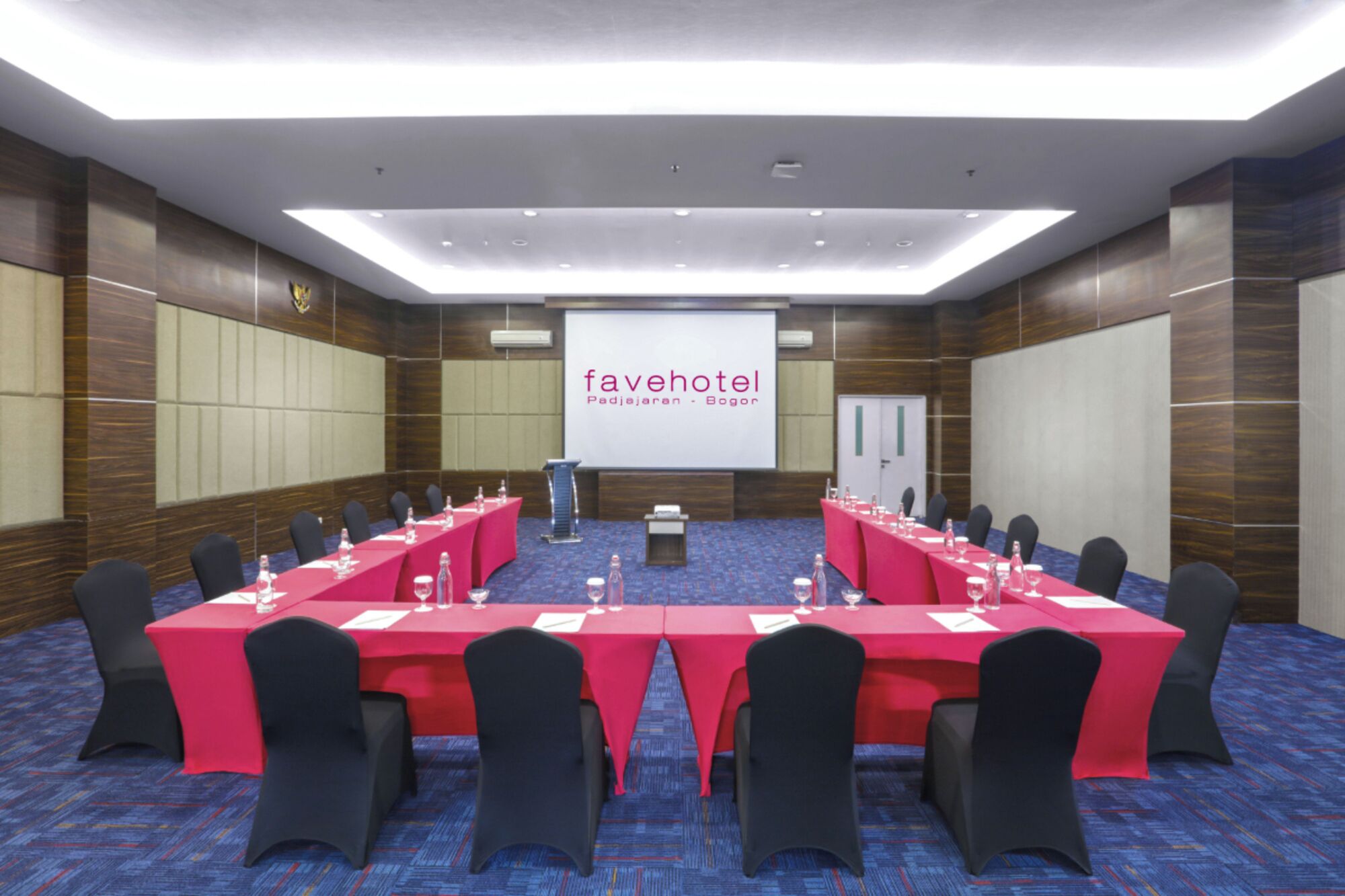 Una sala de conferencias con una larga mesa, sillas y una pantalla para presentaciones.