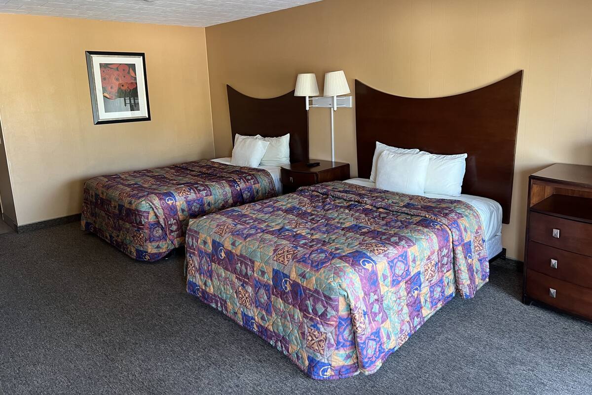Une chambre d’hôtel avec deux lits, une table de chevet, une lampe et une commode.