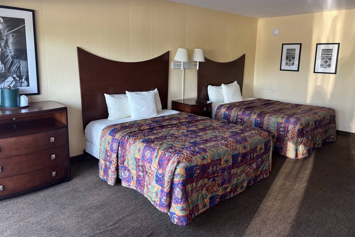 Une chambre d’hôtel avec deux lits, une commode, une lampe et des œuvres d’art encadrées accrochées aux murs.