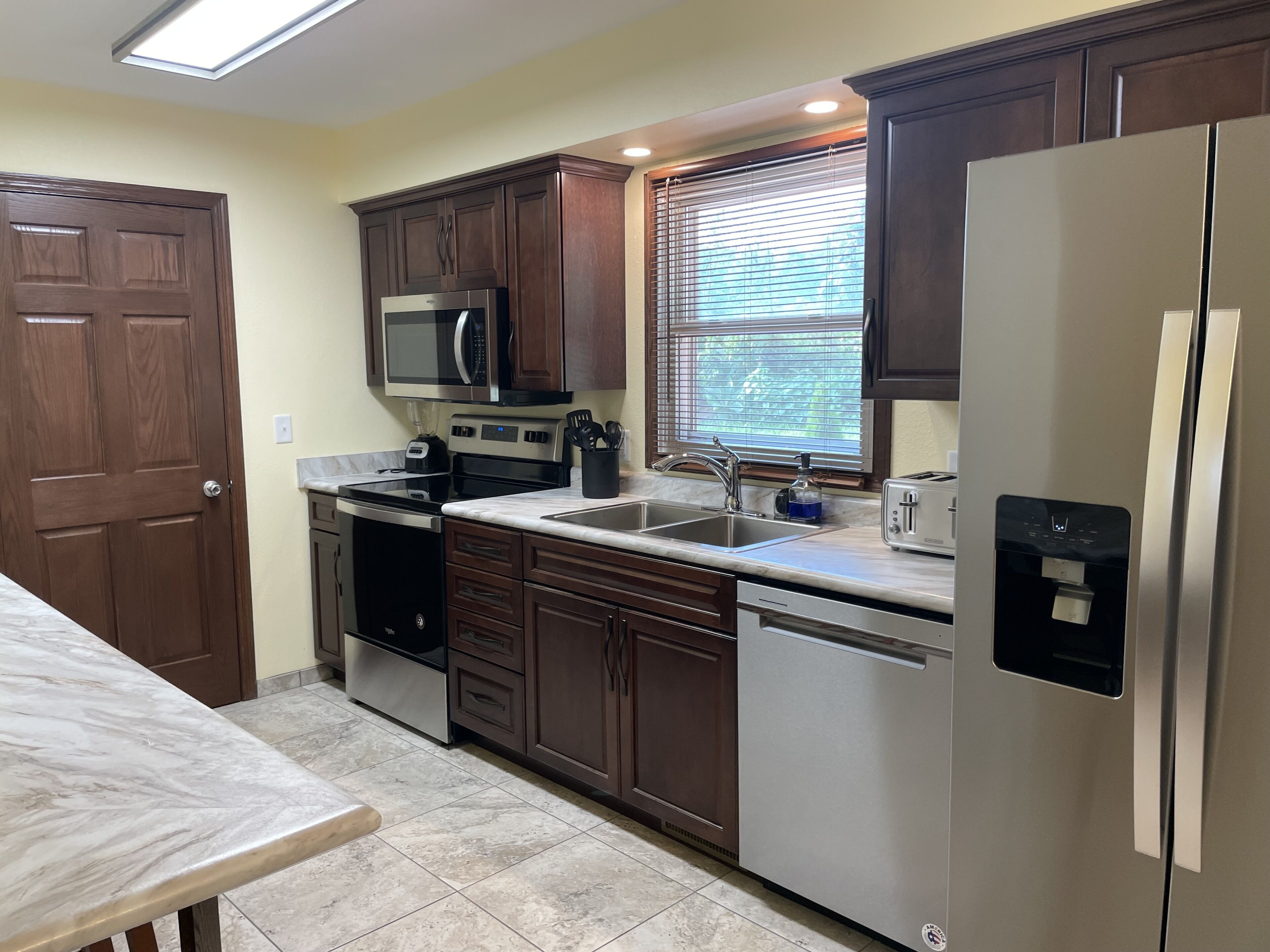 A kitchen with dark wooden cabinets, stainless steel appliances, a built-in microwave, a toaster, and a water dispenser.
