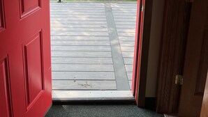 A red door leading to a wooden deck with a metal railing.