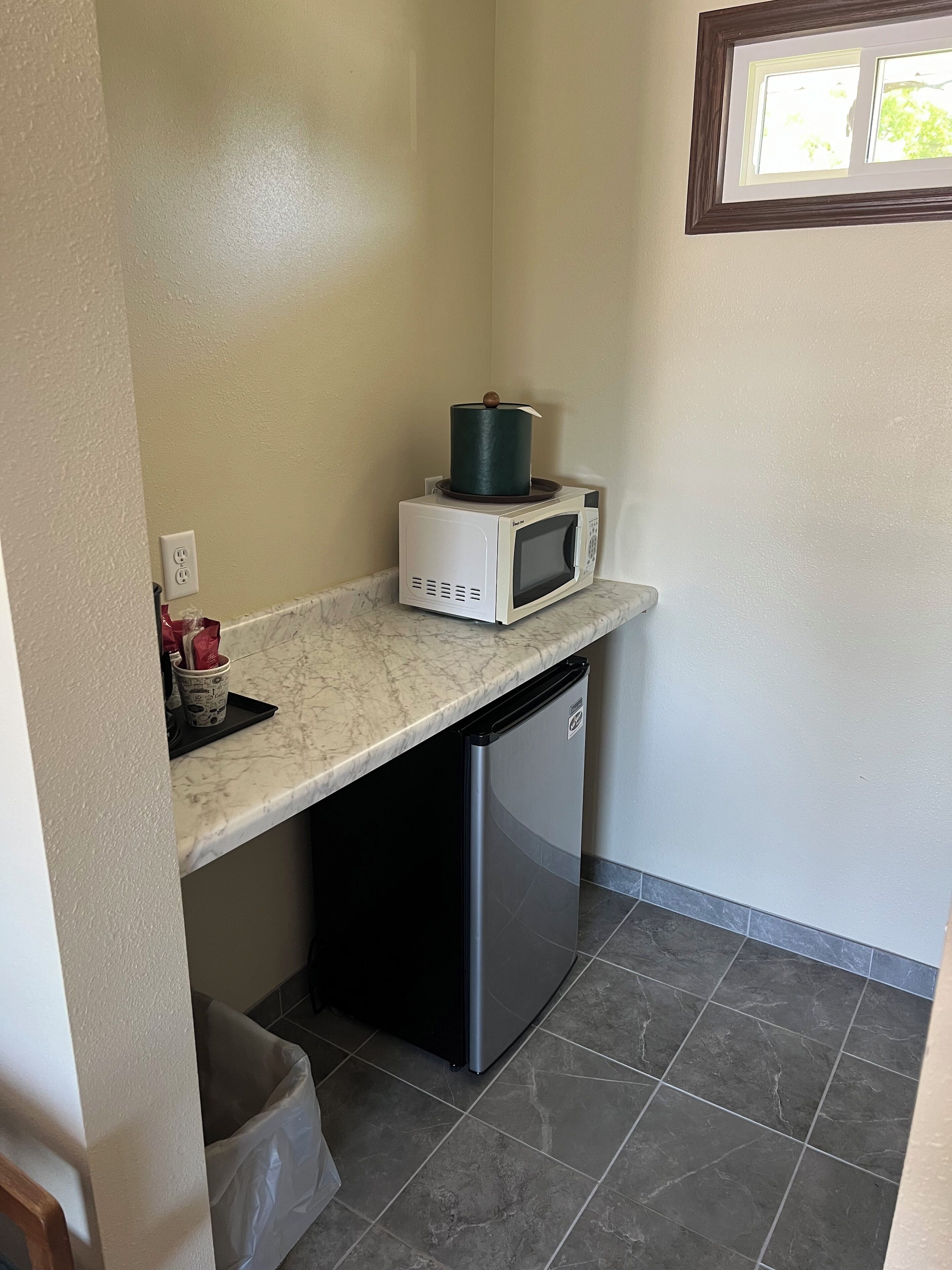 Una cocina compacta con microondas, un refrigerador pequeño y un bote de basura.