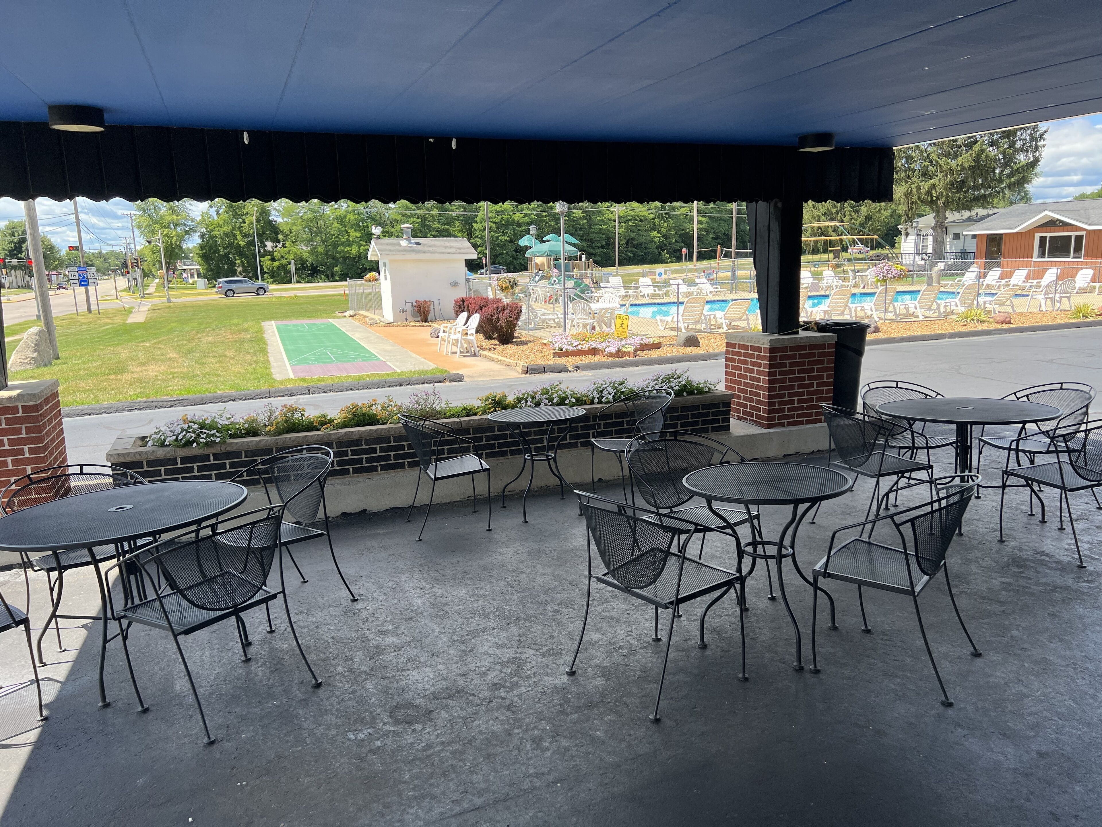 An outdoor patio with metal tables and chairs, a brick wall, and a view of a pool and lawn.