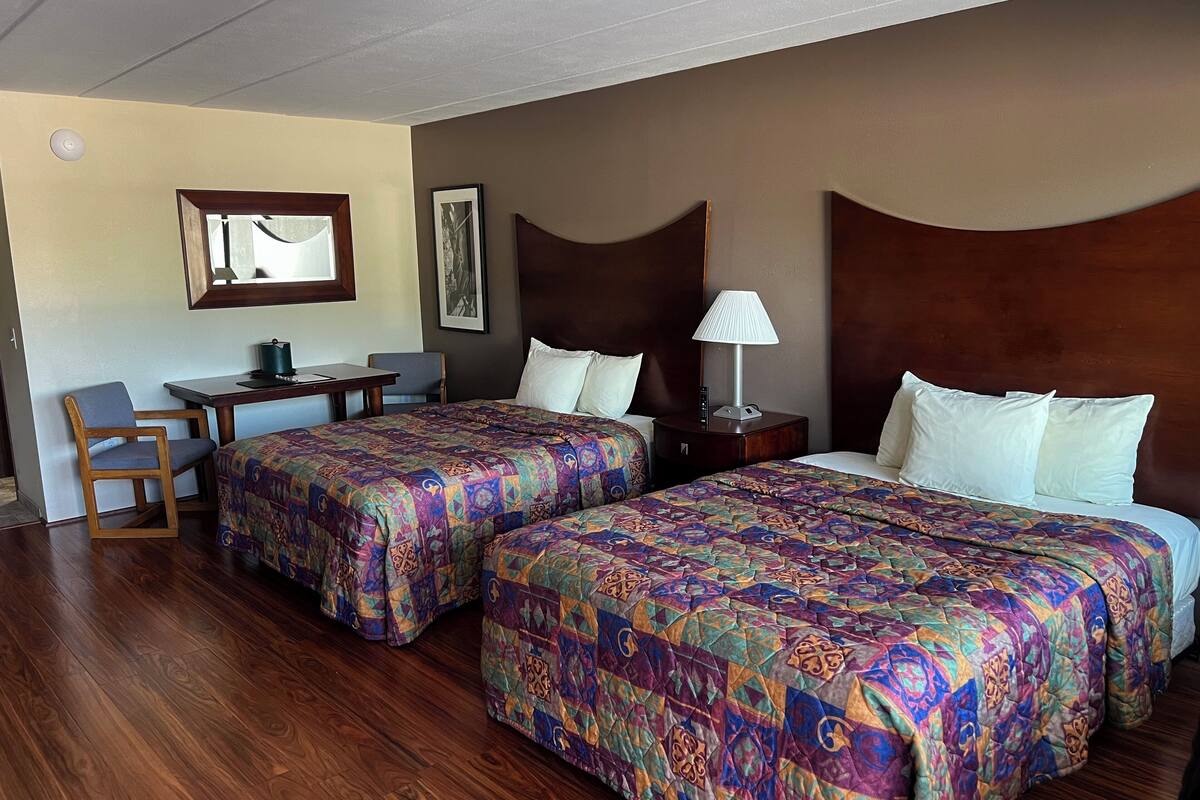 Une chambre d’hôtel avec deux lits, un bureau, une chaise et une table de chevet avec une lampe.