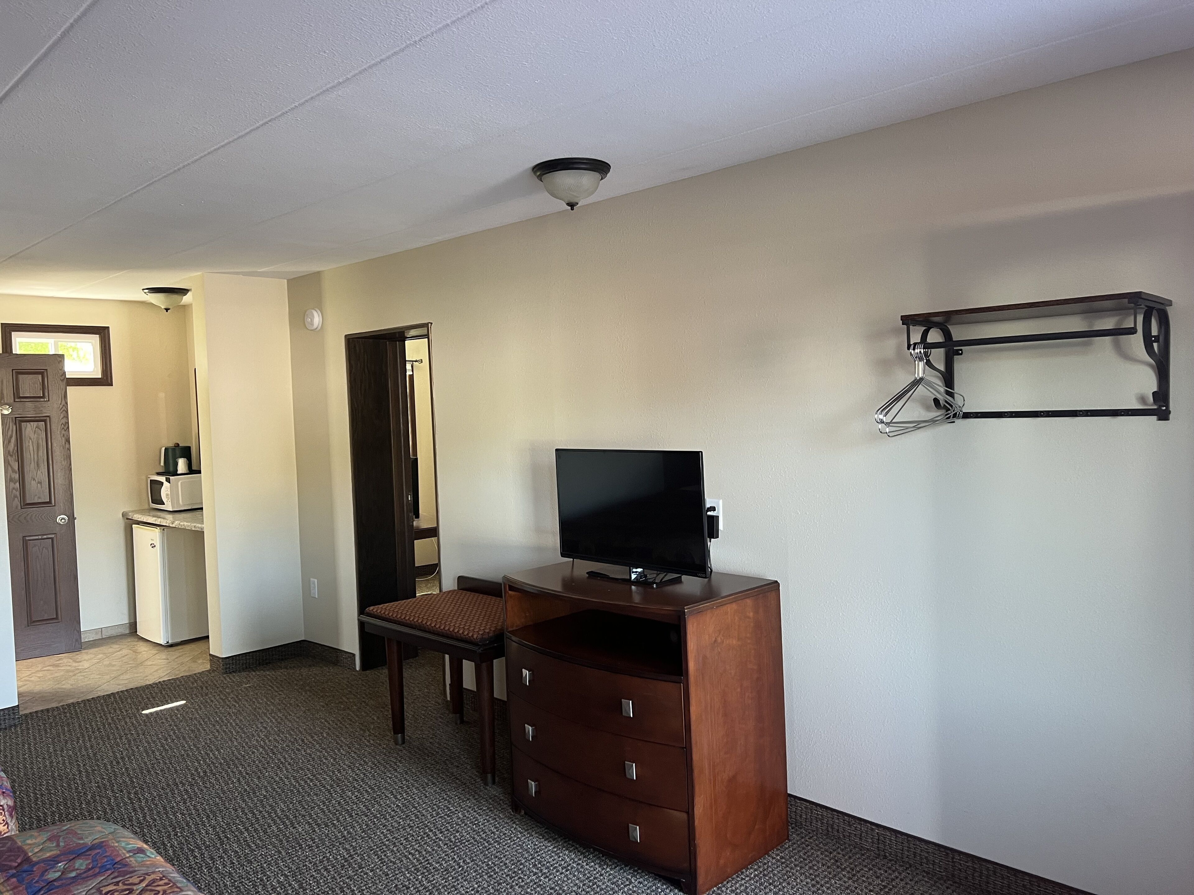 A hotel room with a desk, chair, TV, dresser, and a coat rack.