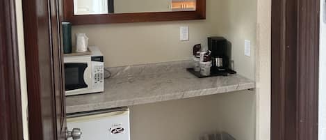 Uma cozinha compacta equipada com micro-ondas, cafeteira e lixeira.