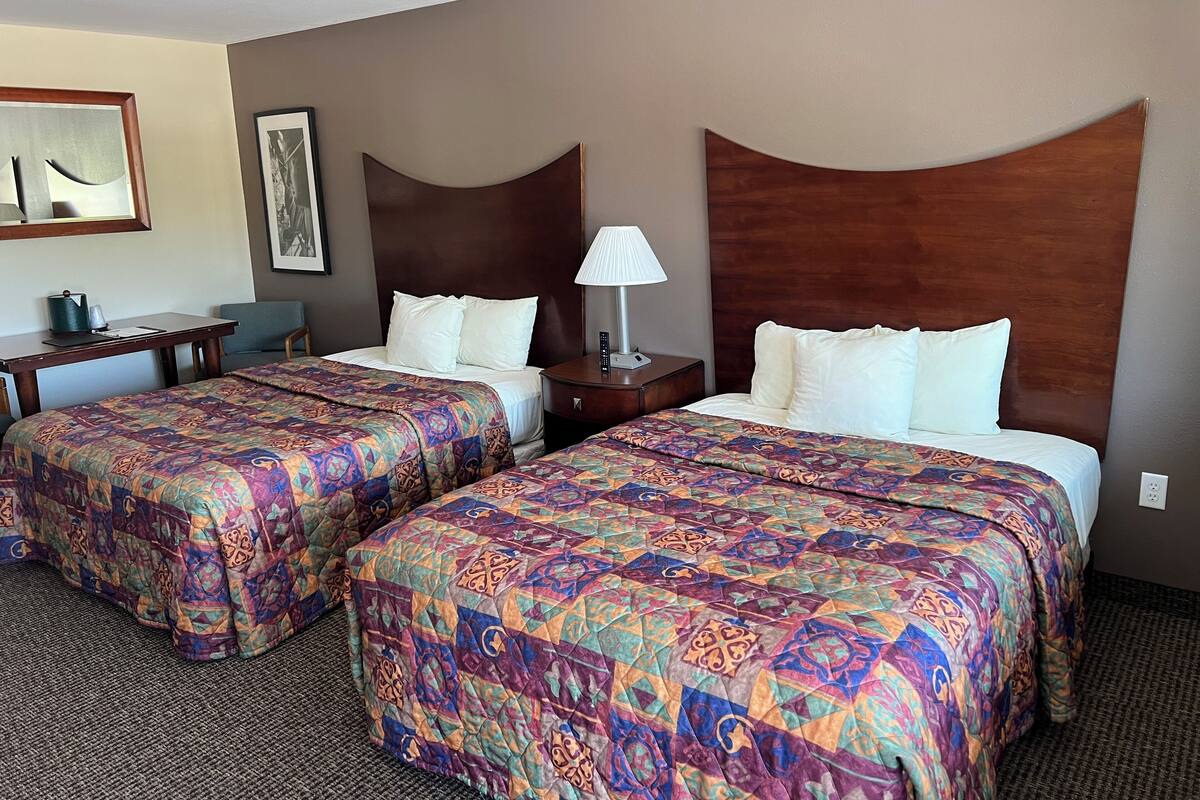 Une chambre d’hôtel avec deux lits, chacun recouvert d’une couvre-lit à motifs, un bureau avec une lampe et une chaise.