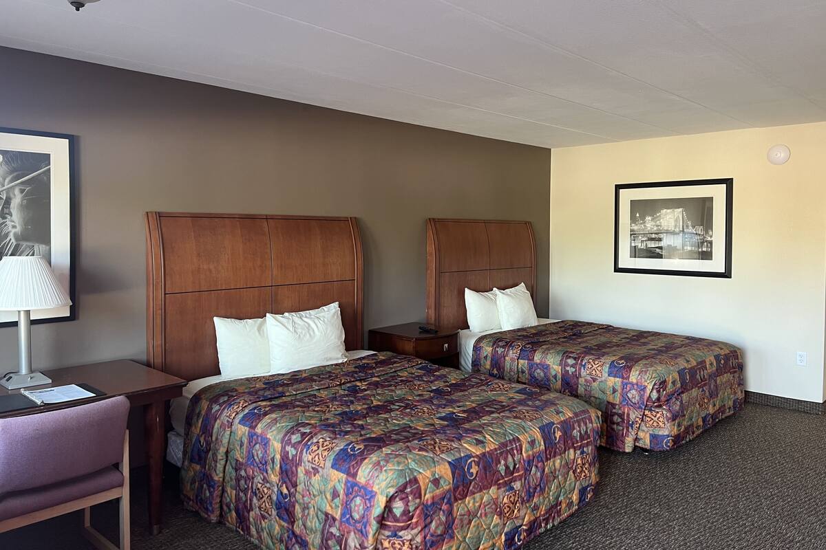Une chambre d’hôtel avec deux lits, un bureau, une chaise et une lampe.