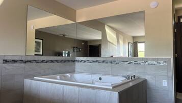 A modern bathroom with a large freestanding bathtub, a large mirror, and a tiled backsplash.