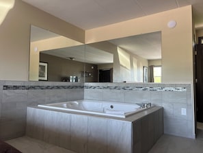 A modern bathroom with a large freestanding bathtub, a large mirror, and a tiled backsplash.