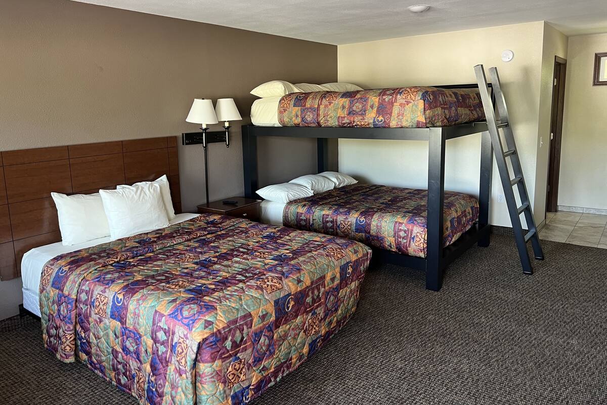 Une chambre d’hôtel avec deux lits, un lit superposé, un bureau avec une lampe et une échelle.