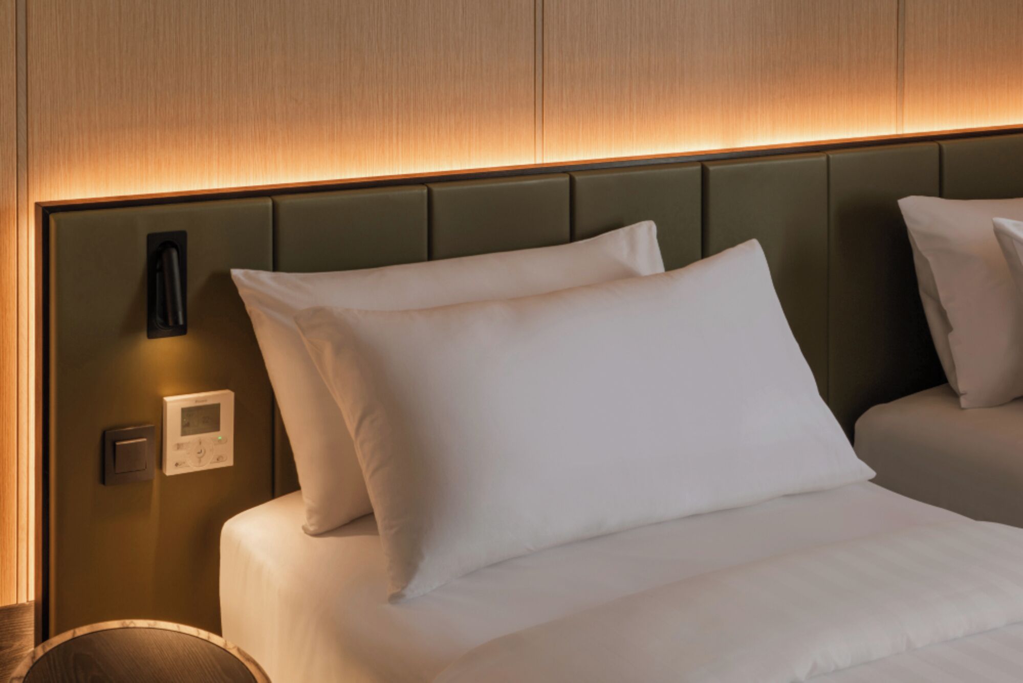 A hotel room with a bed, a control panel, and a wall-mounted light fixture.