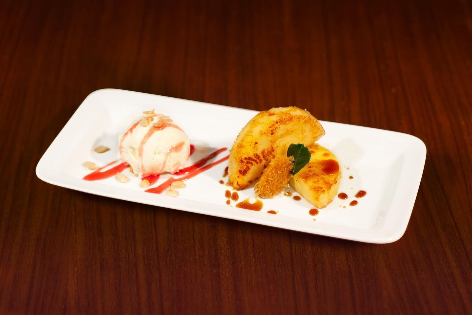 Une assiette à dessert avec de la crème glacée et des bananes caramélisées, le tout présenté sur une assiette rectangulaire blanche.