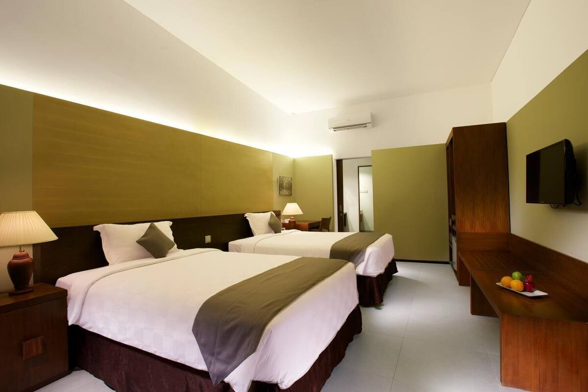 Una camera d'albergo con due letti, una televisione, una scrivania con della frutta e uno specchio.