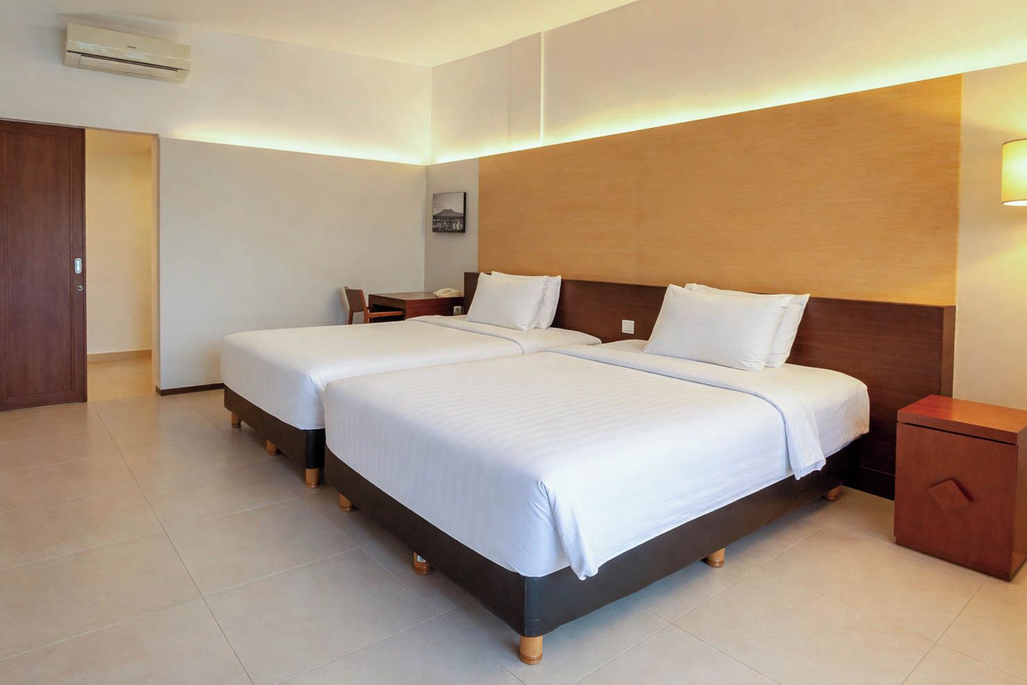 Ein Hotelzimmer mit zwei Betten, einem Schreibtisch, einem Stuhl, einem Nachttisch und einer Klimaanlage.