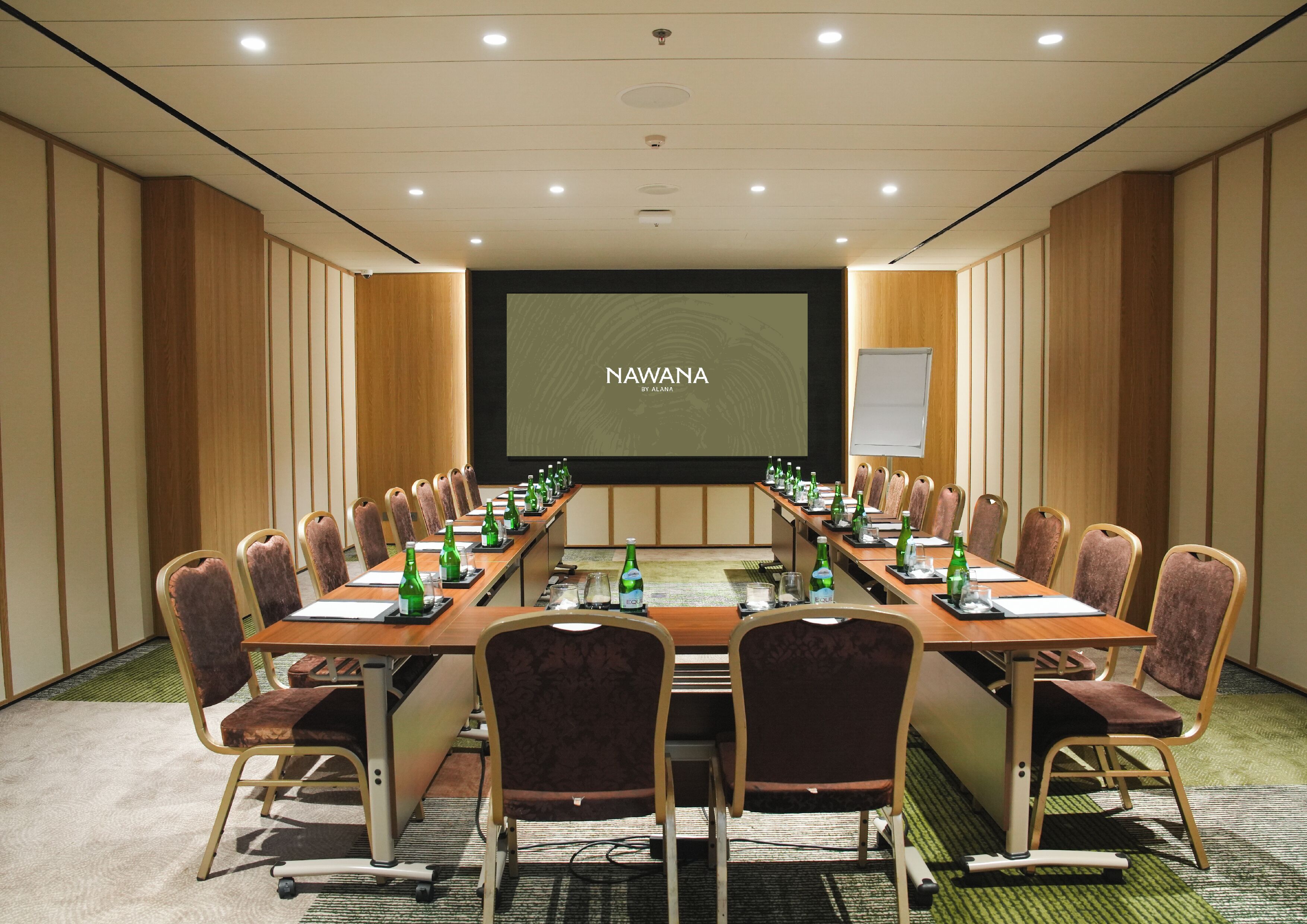 Una sala de conferencias con una larga mesa, sillas, una pantalla para proyector y una pizarra.