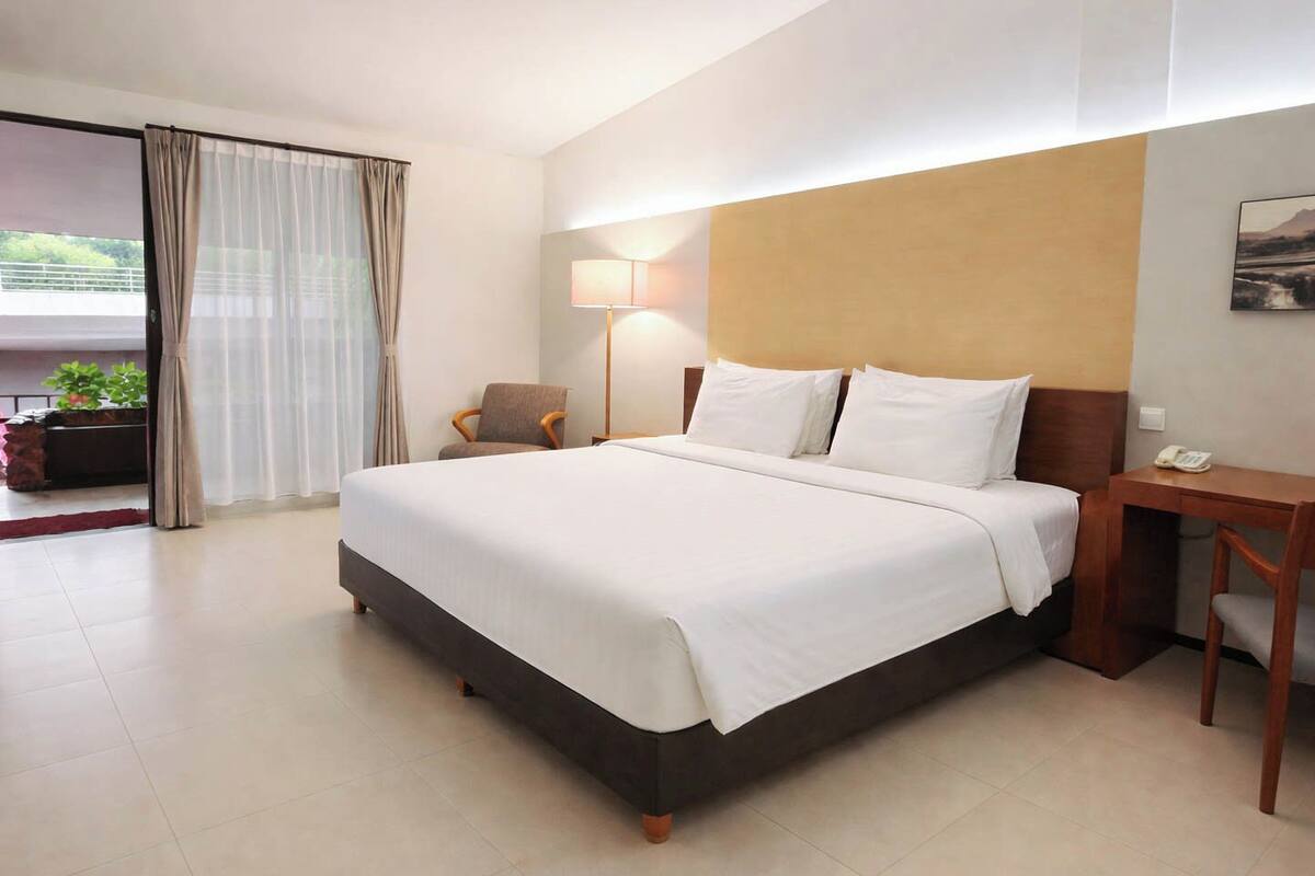 Una camera d'albergo con un letto, una scrivania, una sedia, una lampada e vista sull'esterno.