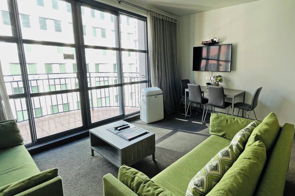 A modern living room with a green sofa, a small coffee table, and a TV mounted on the wall.