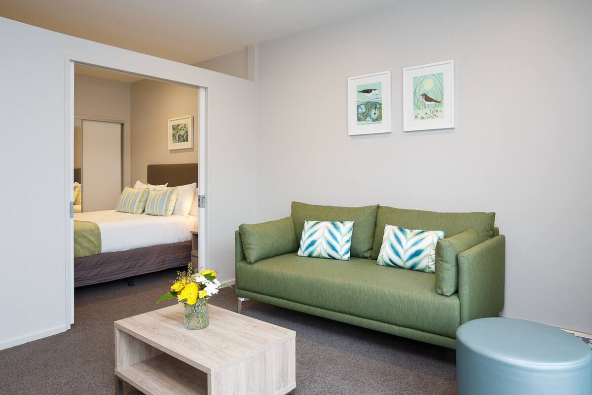 A modern room with a bed, a green sofa, a coffee table, and two framed pictures on the wall.