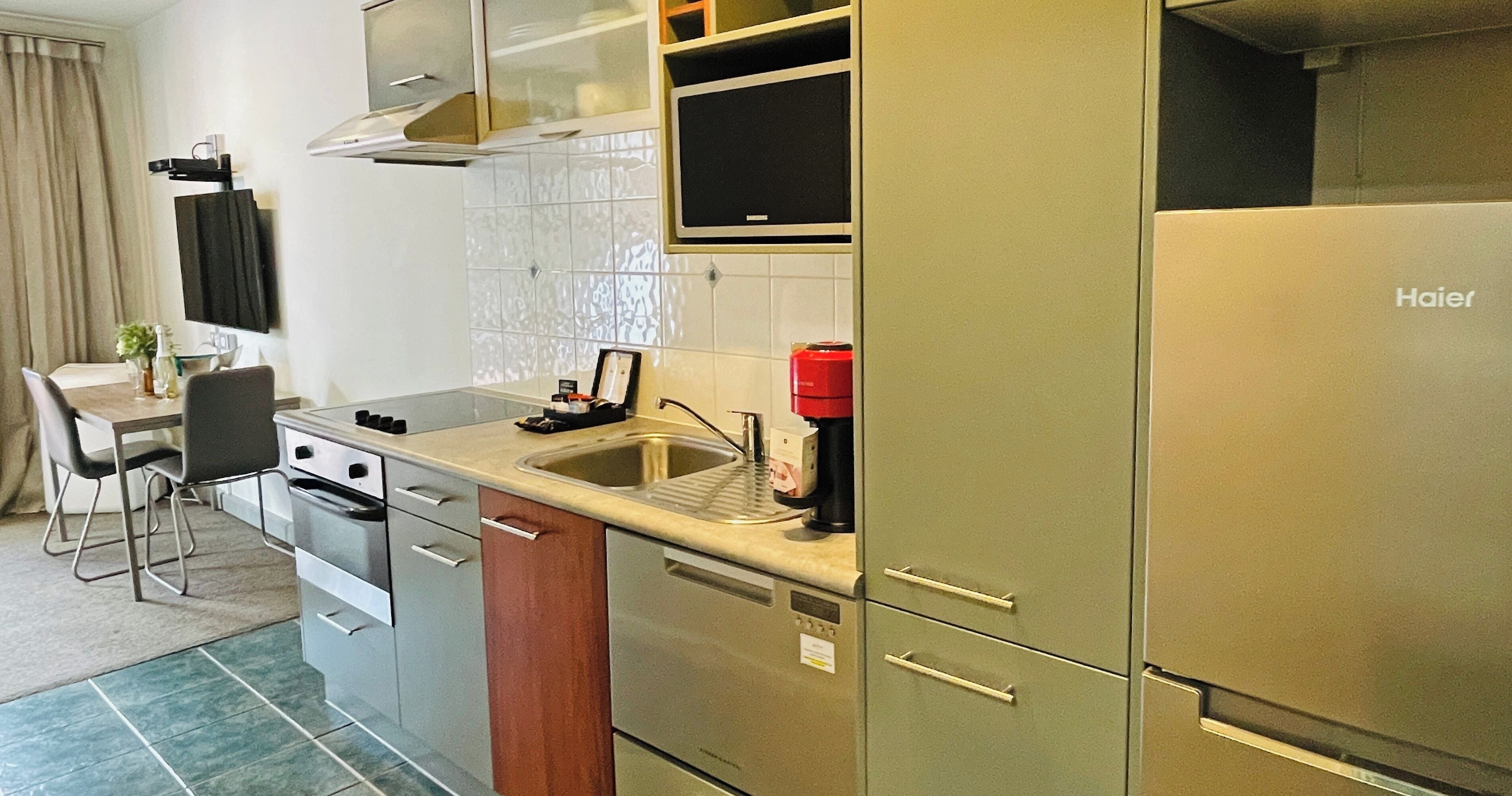 A compact kitchen with a stainless steel refrigerator, a built-in microwave, and a sink. There is a dining area with a chair and a table.