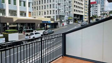 A modern building with multiple floors, a gated entrance, and a street with cars and a pedestrian.