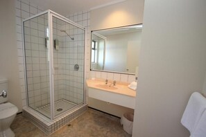 Une salle de bain avec une douche à parois de verre, un lavabo avec un miroir et des toilettes.