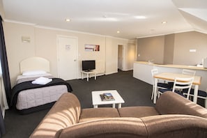A hotel room with a bed, a sofa, a small table with a book, a TV, and a kitchenette area.