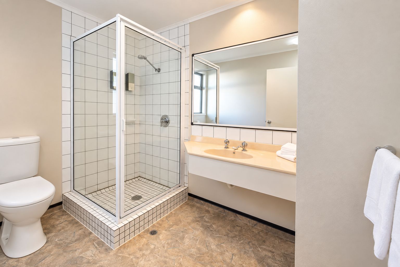 Un baño moderno con ducha envuelta en vidrio, inodoro, lavamanos con espejo y perchero para toallas.