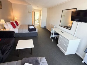 A hotel room with a bed, a desk, a chair, a TV, and a window.
