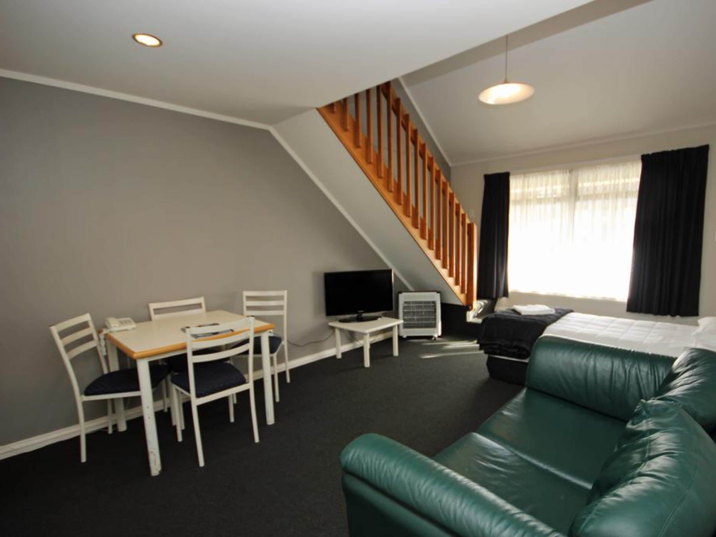 A modern living room with a green leather sofa, a dining table with chairs, a TV, and a staircase.