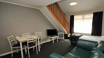 A modern living room with a green leather sofa, a dining table with chairs, a TV, and a staircase.