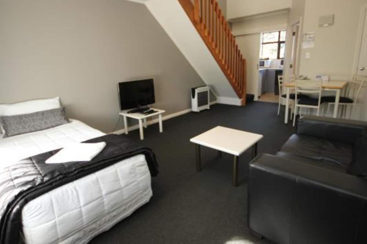 A hotel room with a bed, a TV, a small table, a sofa, and a staircase leading to a kitchen area.