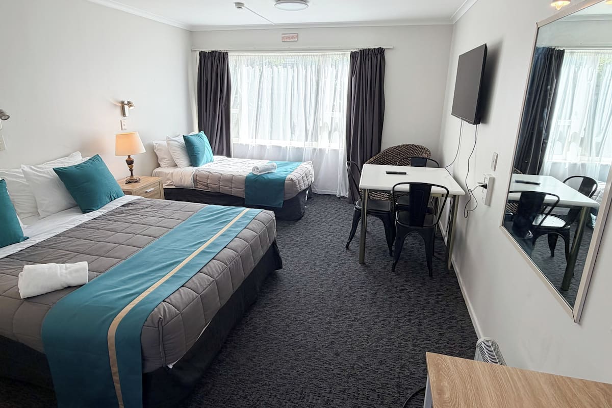 A hotel room with two beds, a desk, a chair, a TV, and a window with curtains.