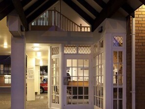 Une entrée d’immeuble avec un escalier menant au deuxième étage, un garage avec une voiture rouge et une enseigne indiquant un service de location de voitures.