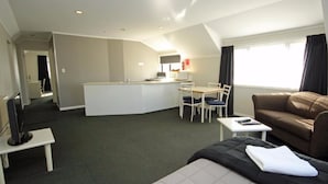 A hotel room with a bed, a sofa, a TV, a desk, and a kitchenette. - Champers Motor Inn (Lower Hutt)