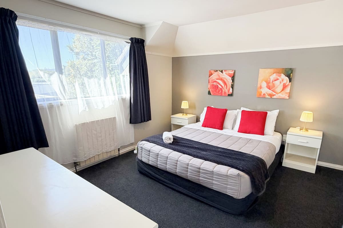 A hotel room with a bed, bedside tables, a desk, and two paintings on the wall.