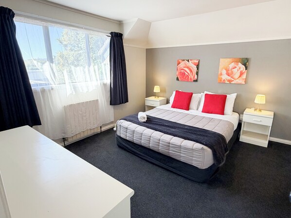 Une chambre d’hôtel avec un lit, des tables de chevet, un bureau et deux tableaux accrochés au mur.