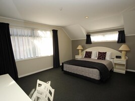 Habitación de hotel con cama, dos mesitas de noche, una silla, ventana con cortinas e iluminación en el techo.
