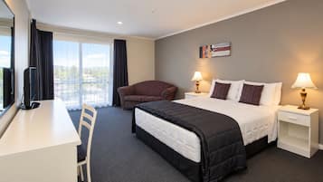 Une chambre d’hôtel comprenant un lit, un bureau, une chaise, un canapé, deux tables de chevet avec des lampes et une fenêtre avec des rideaux.