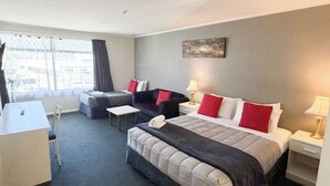 A hotel room with a bed, two sofas, a desk, and a window with curtains. - Champers Motor Inn (Lower Hutt)