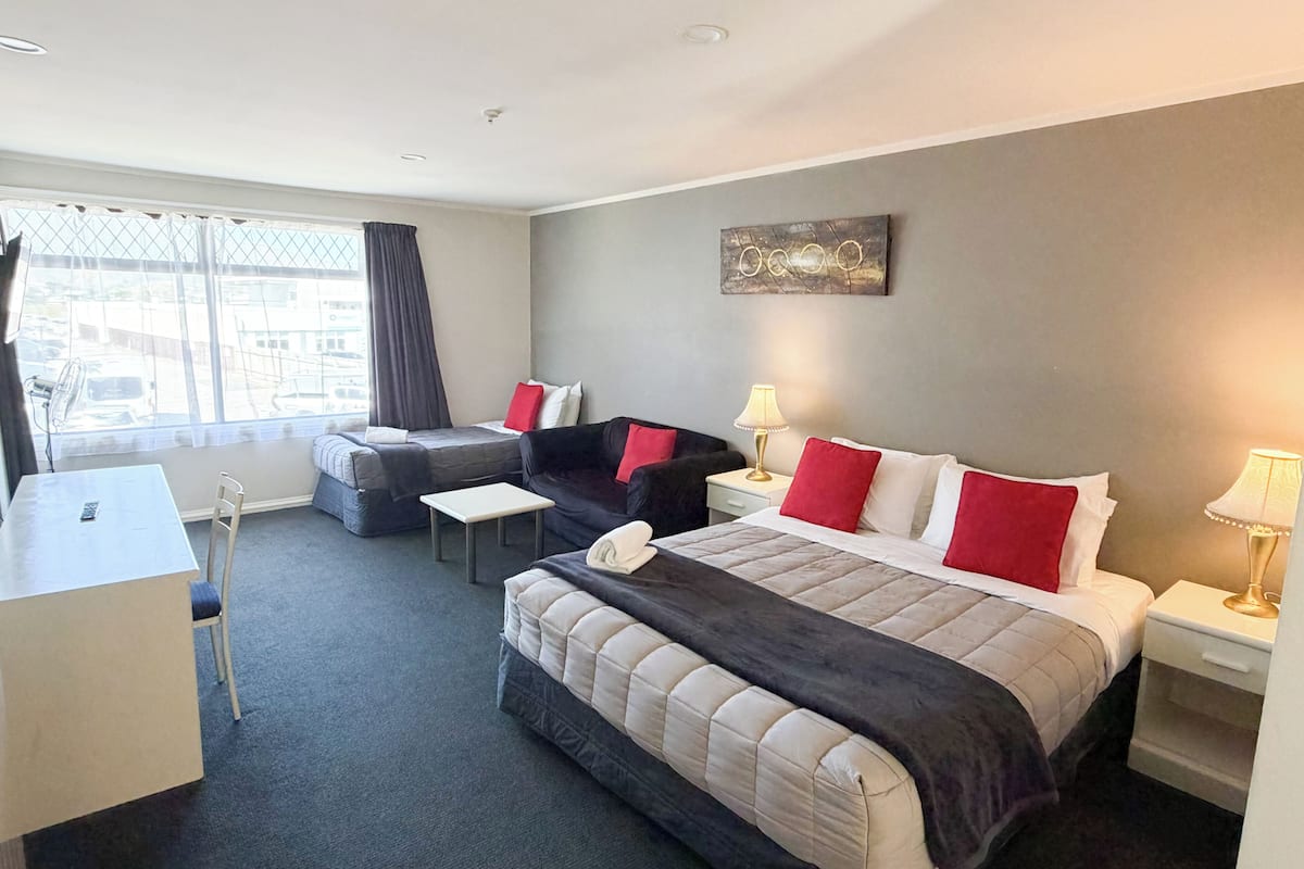 A hotel room with a bed, two sofas, a desk, and a window with curtains.