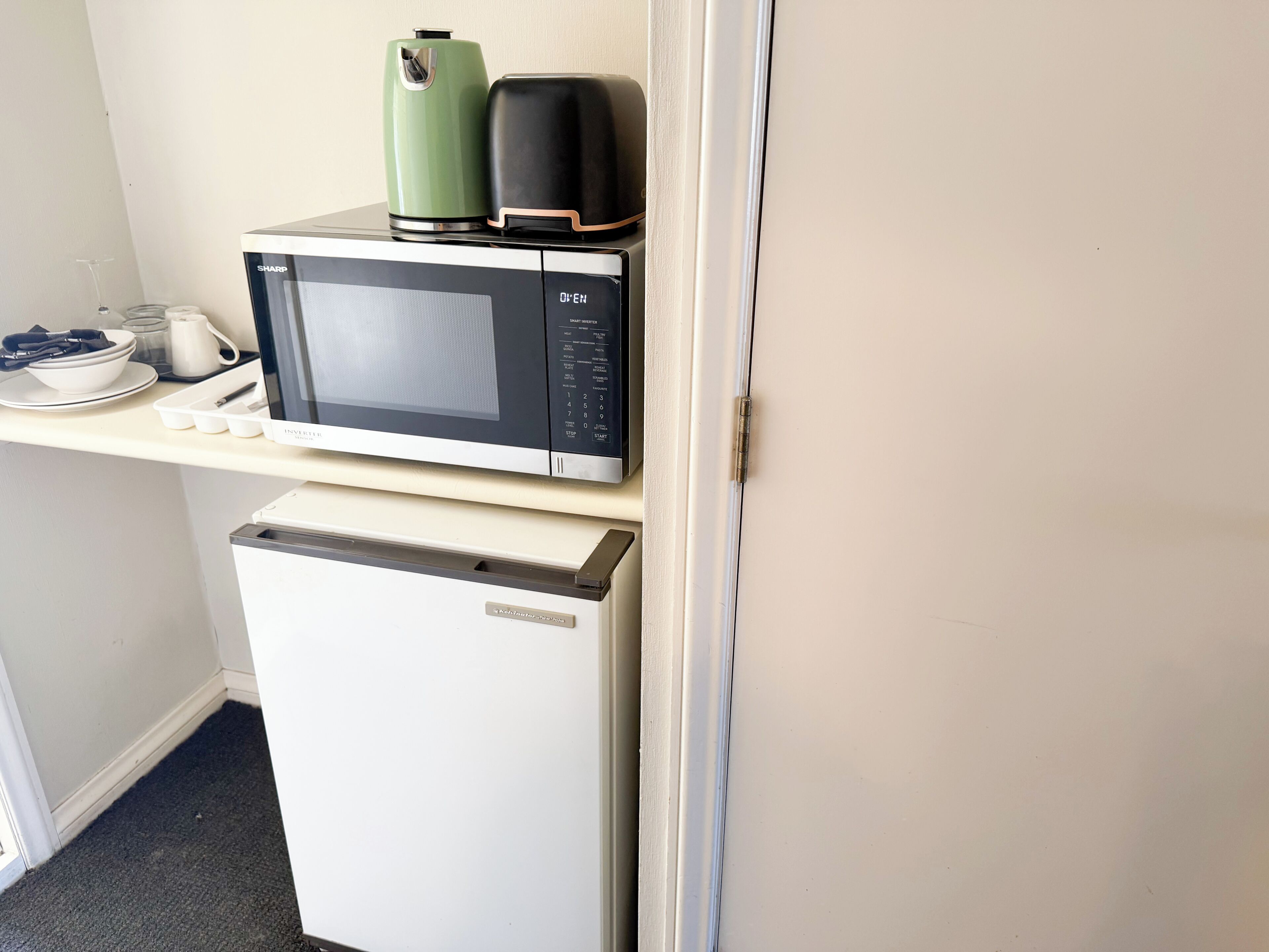Una kitchenette compacta con microondas, un refrigerador pequeño y una tetera.