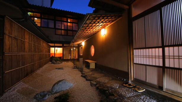 Un edificio japonés tradicional con fachada de madera, un sendero de piedra y un banco de madera.