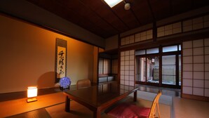 Una habitación japonesa tradicional con suelo de tatami, una mesa baja, una silla y puertas correderas.