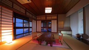 Una habitación tradicional japonesa con suelo de tatami, una mesa de madera, puertas correderas y vistas al exterior.