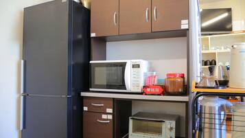Cocina compacta con refrigerador, microondas, tostadora y cafetera sobre la encimera.
