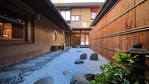 Un patio japonés tradicional con un sendero de piedra, paredes de madera y un edificio de madera con puertas correderas.