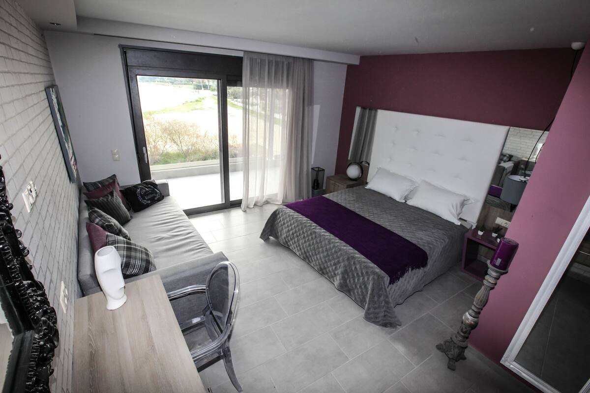 Una habitación de hotel moderna con cama, escritorio y silla. Cuenta con un ventanal con vistas al exterior.